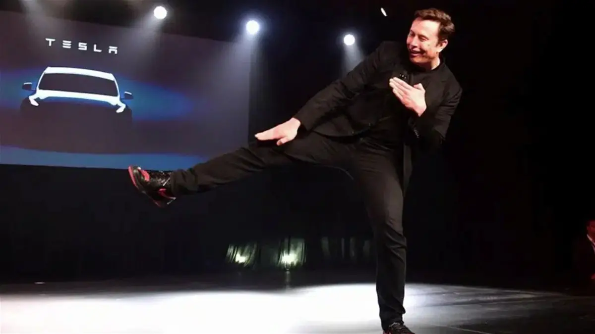 Elon Musk kicking in the air during a Tesla event
